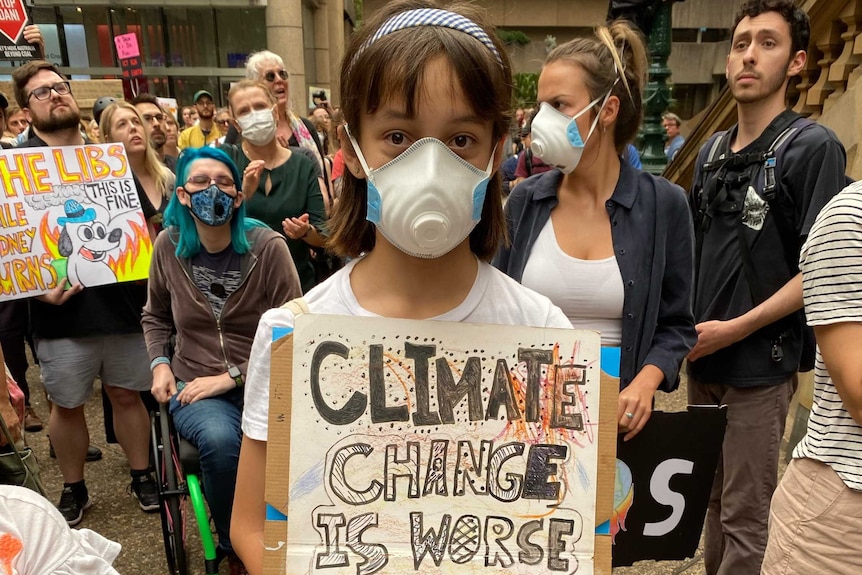 A girl with a face mask holds a climate protest sign.
