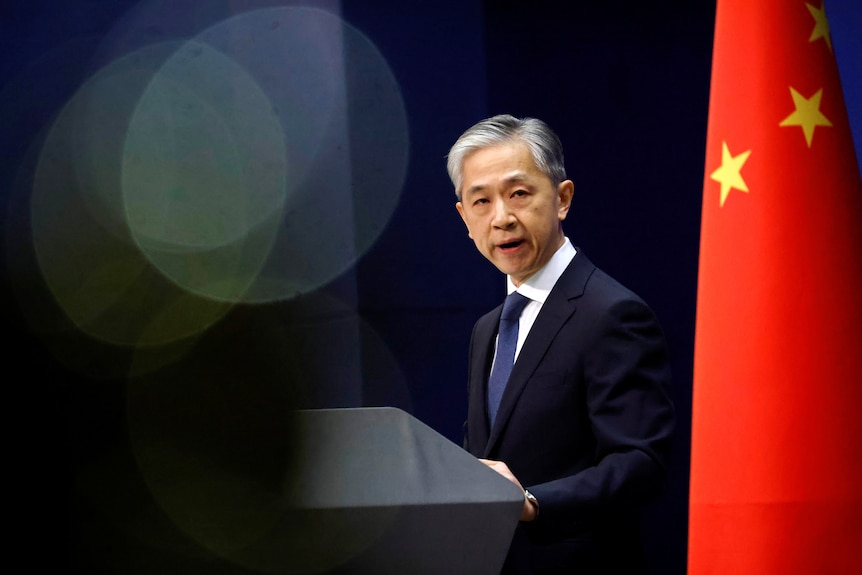 China's foreign ministry spokesman Wang Wenbin speaks during a press conference in 2020, flanked by a Chinese flag.