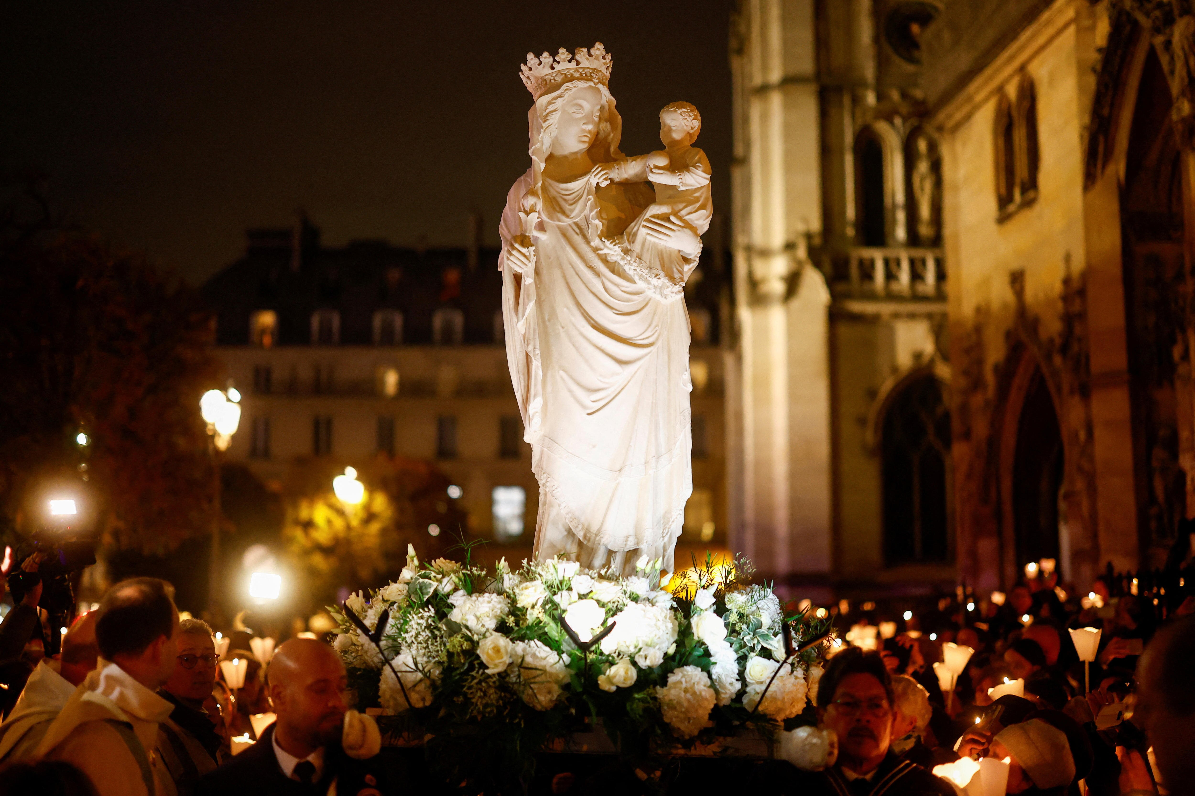 A white stone statue sculpture of the Virgin Mary carrying a child on a bed of white roses