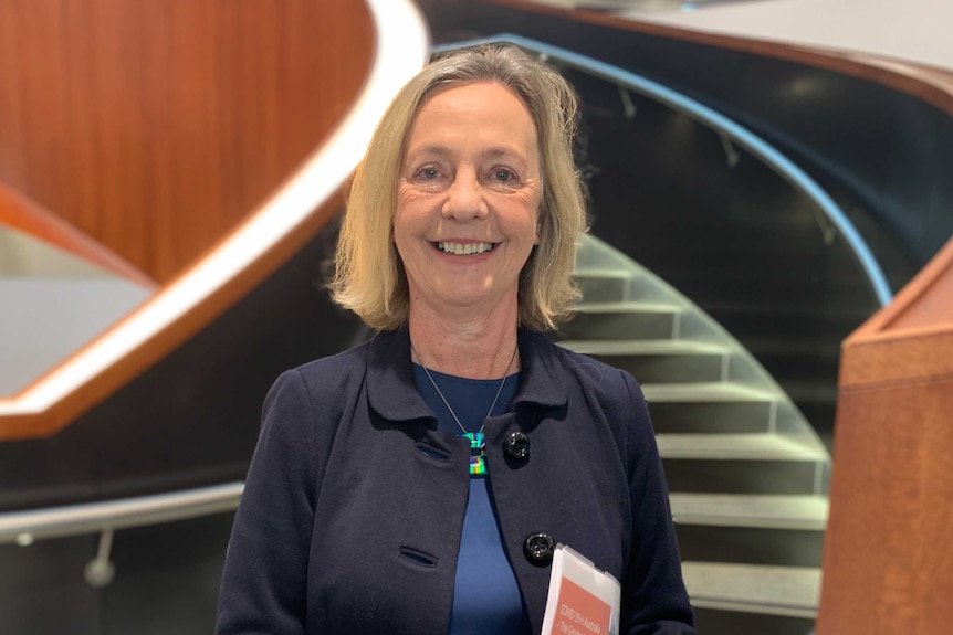 Professor Marian Baird smiling while standing in front of a spiral staircase.