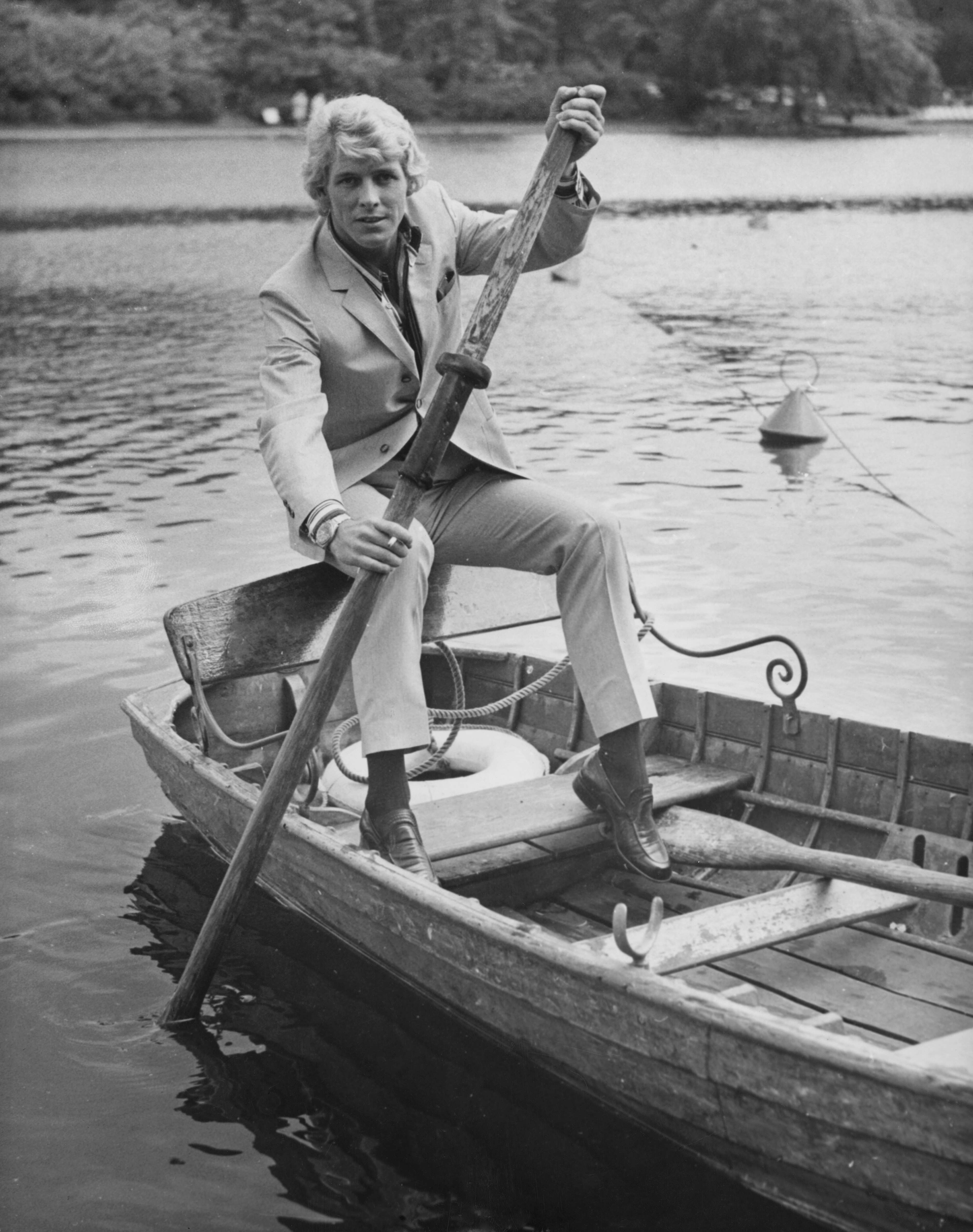 Black and white photo of Tony Bonner in a 70s style suit, rowing a boat on a lake