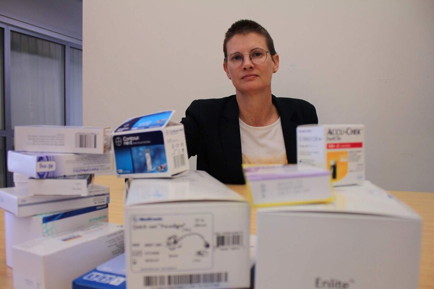 A woman sits behind a large pile of pharmaceutical boxes