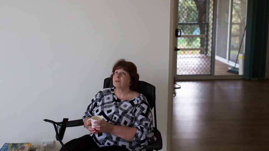 Helen Smith casts her eyes skyward as she clasps a cup of coffee, sitting on a camp chair in her empty living room.
