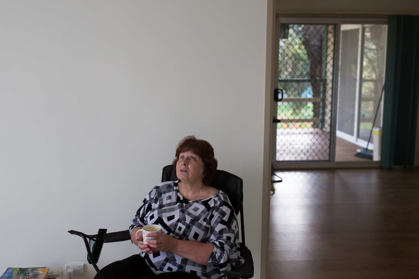 Helen Smith casts her eyes skyward as she clasps a cup of coffee, sitting on a camp chair in her empty living room.