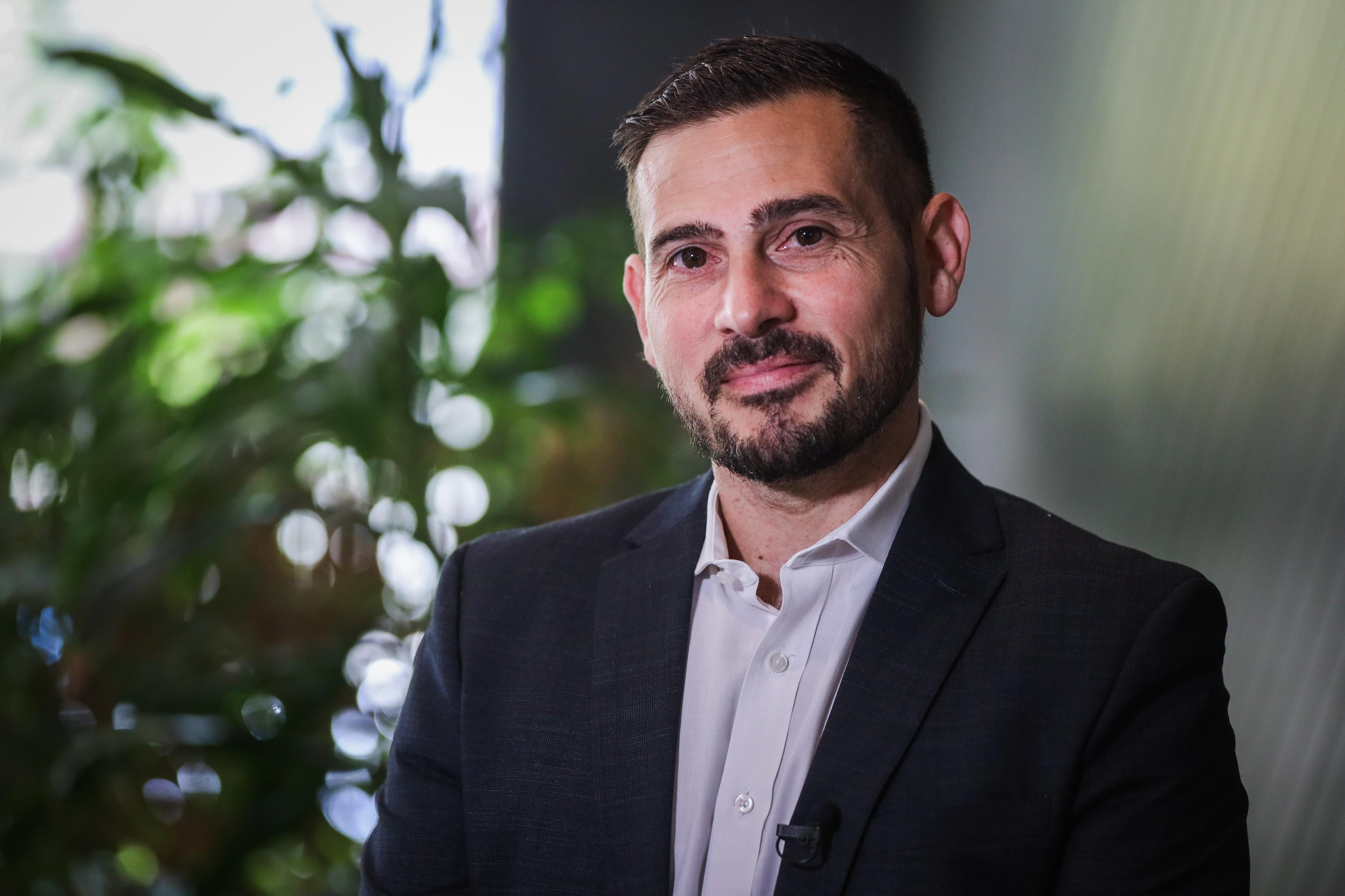 An elegantly dressed man poses against a background of greenery. 