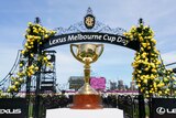 A solid gold trophy sits on a table in front of an archway with "Melbourne Cup Day" on it at Flemington race