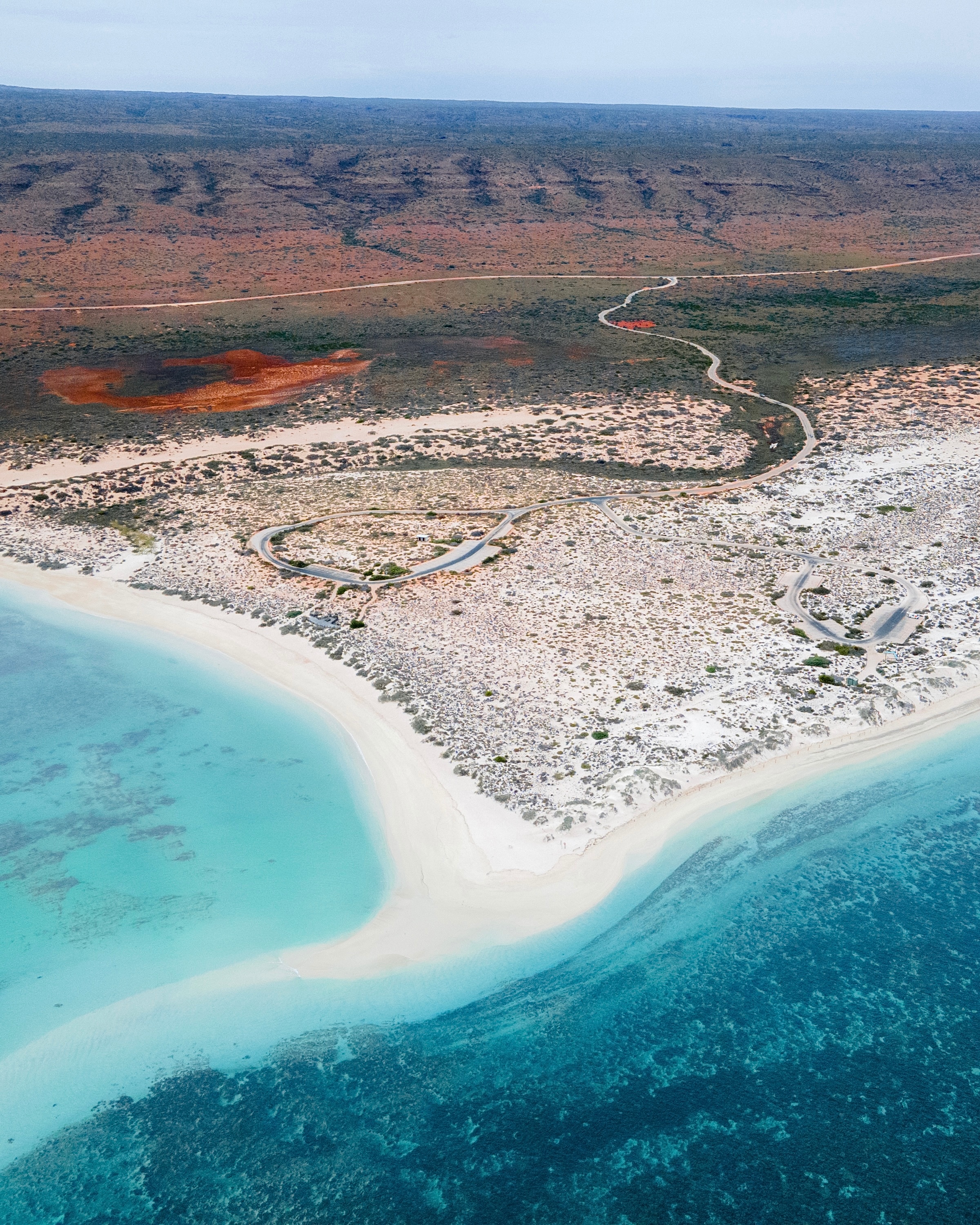 A coastline is seen from above with white sand beaches and clear blue water. 