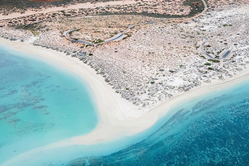 A coastline is seen from above with white sand beaches and clear blue water. 