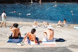 a group of swimmers lying on towels beside a rock pool in sydney