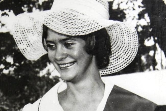 Black and white image of a young woman smiling in a broad-rimmed hat.