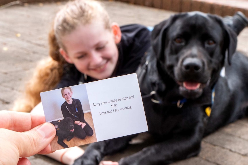 A card with the words "sorry I am unable to stop and talk. Oynx and I are working" written on it with a young girl and dog.