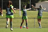 Woman standing with her arm open waiting to be embraced by teammates after scoring a goal in soccer