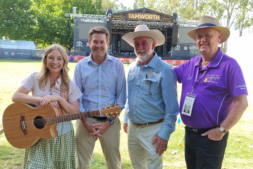 Four people standing in a park with a stage in the background