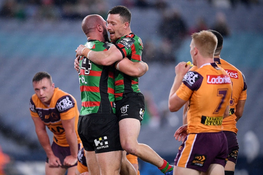 Two South Sydney NRL players embrace as they celebrate a try as Brisbane Broncos players look on.