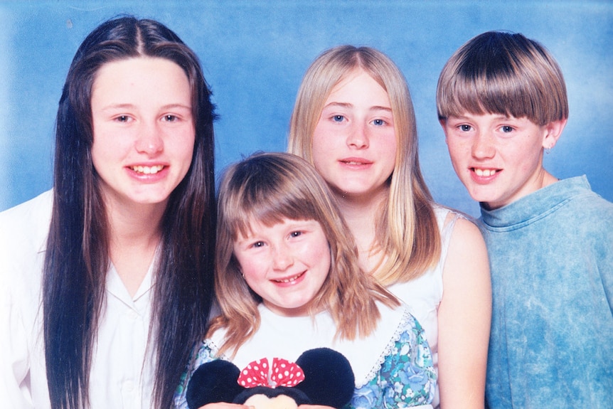 A family portrait of three young girls and a boy against a blue studio backdrop.