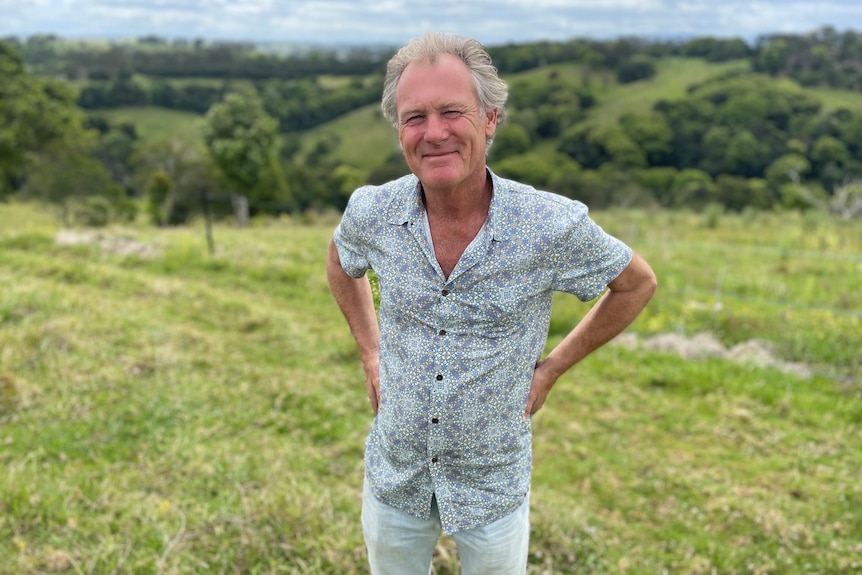 Photo of a man smiling in front of rolling green hills.