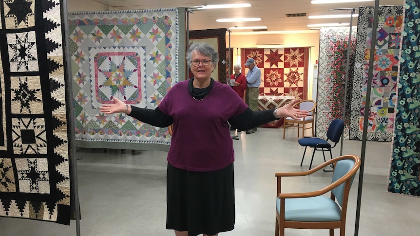 Woman stands among hanging quilts