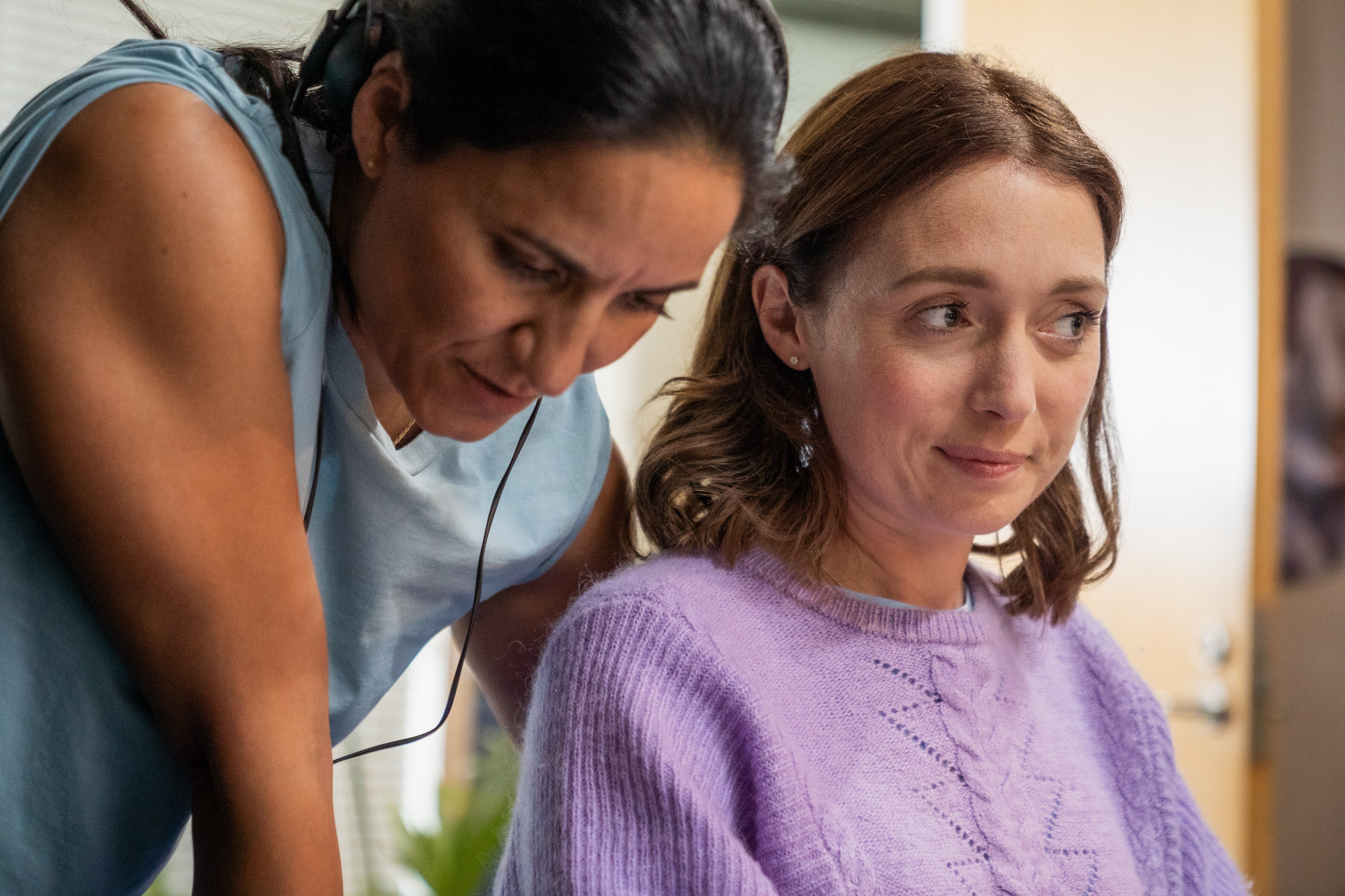 A woman leans over the shoulders of another woman, looking concerned.
