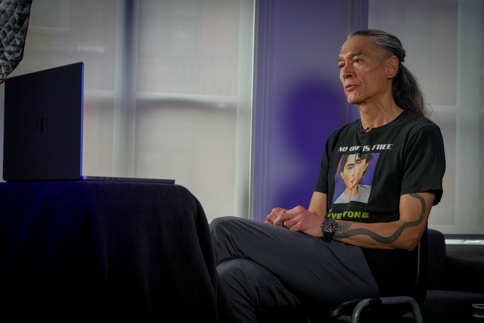 A man sits in front of a laptop in a room with purple walls. 