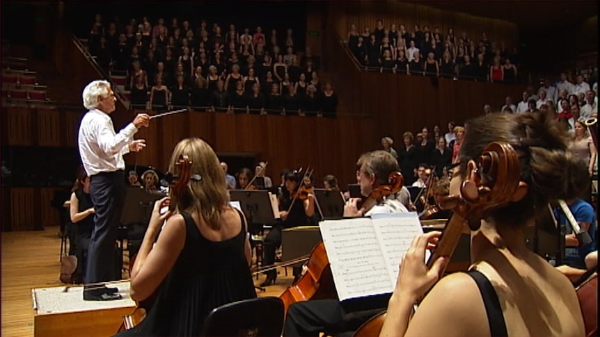 Former Australian Prime Minister Bob Hawke conducting and orchestra and choirs on the stage of the Sydney Opera House.