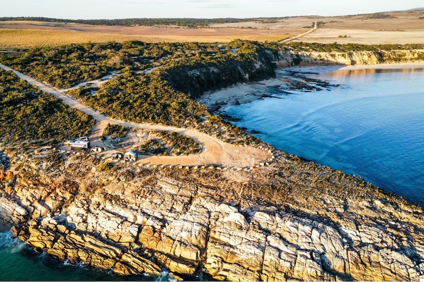 Drone photo of rocky coastal peninsula, with sandy road through green shrubs leading to the end, finishing in a loop