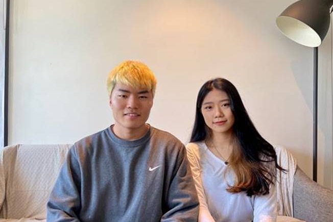 Shavhin (left) and Yehvhin Ahn sit on a couch facing the camera.