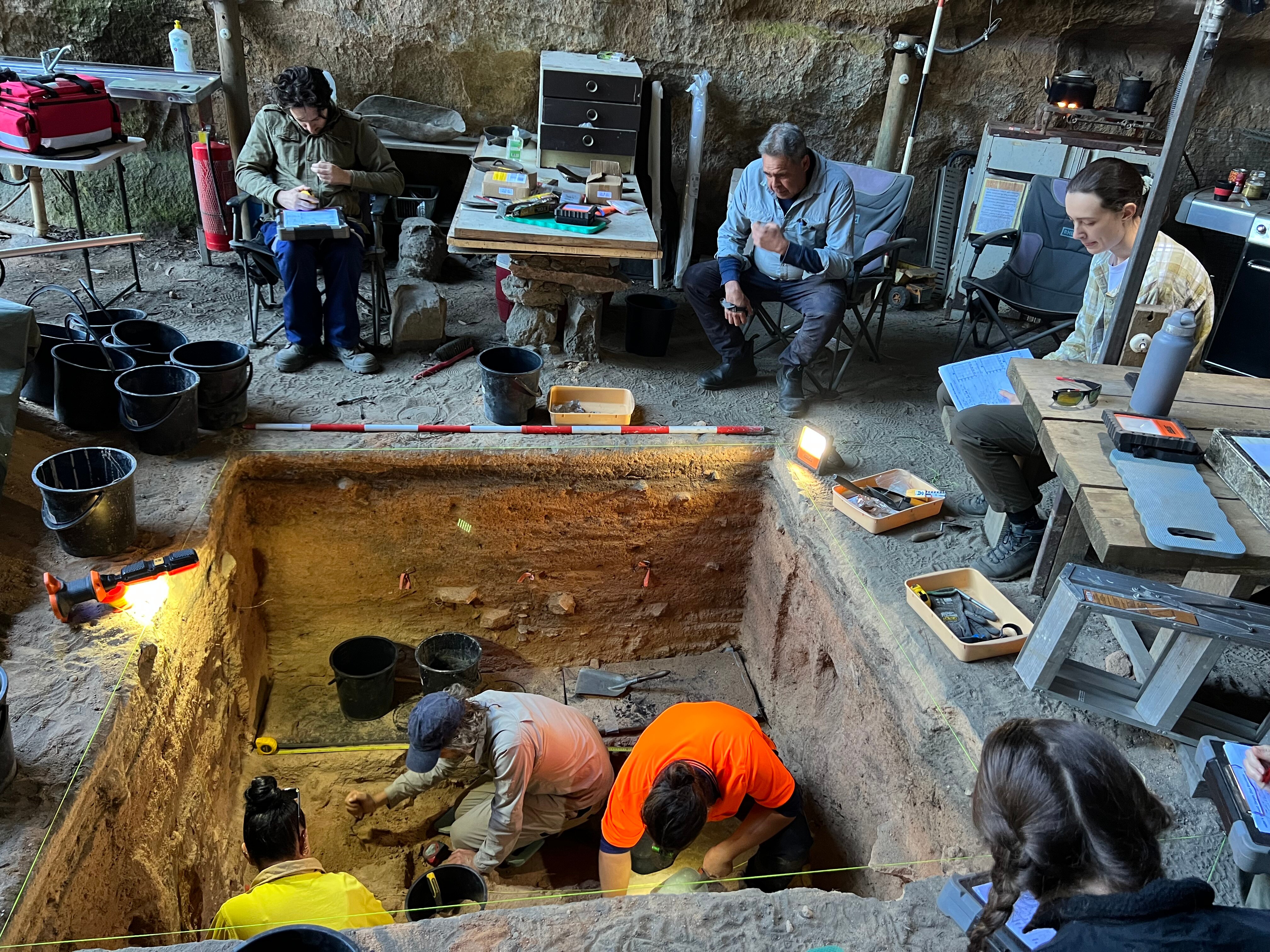 Archaeologists work in a square hole dug into the ground.