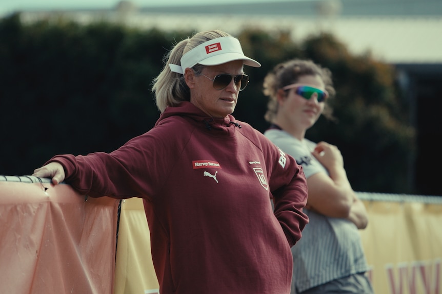 Tahnee Norris leans on a fence, wearing a visor and sunglasses.