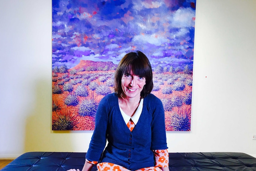 Sarah Brown sitting in front of an artwork that she painted