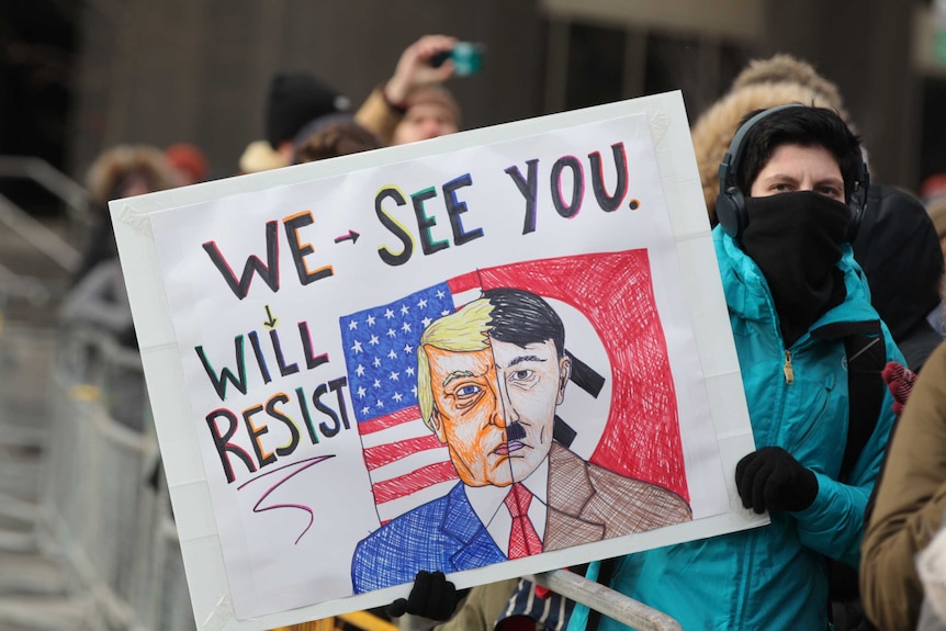 A protester holds a sign comparing Donald Trump to Adolf Hitler.