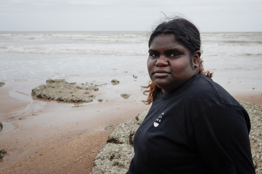 a young aboriginal woman standing on a beach in front of the ocean