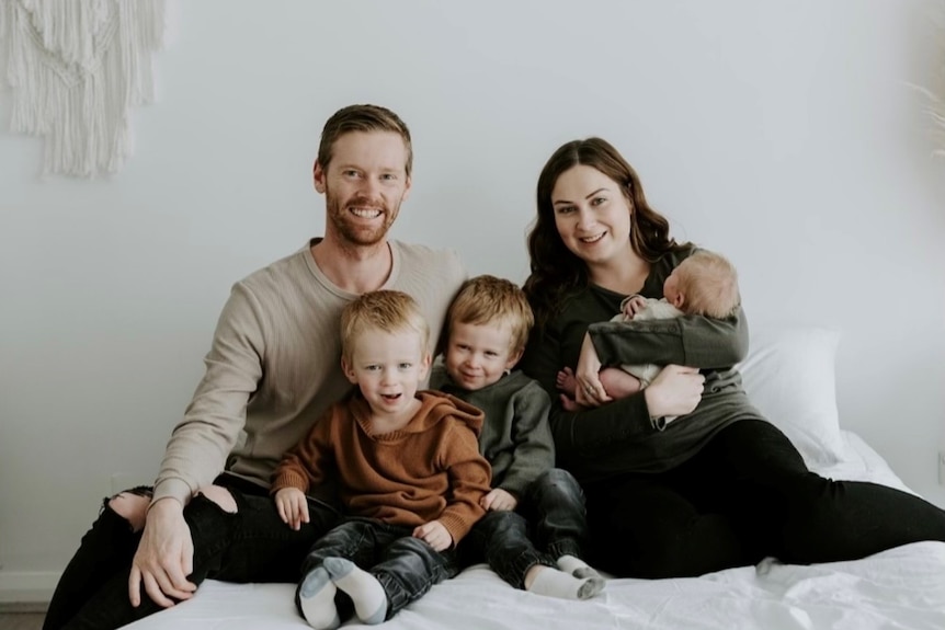 Ryan and and his wife sit on a bed, she is holding a baby and there are two twin boys between them