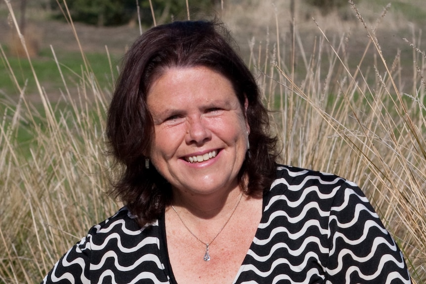 A smiling, dark-haired  woman standing in front of a field of tall grass.