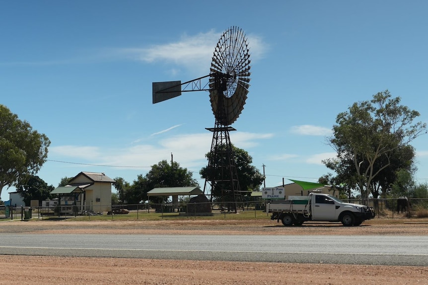 a windmill next to a road and a parked white ute
