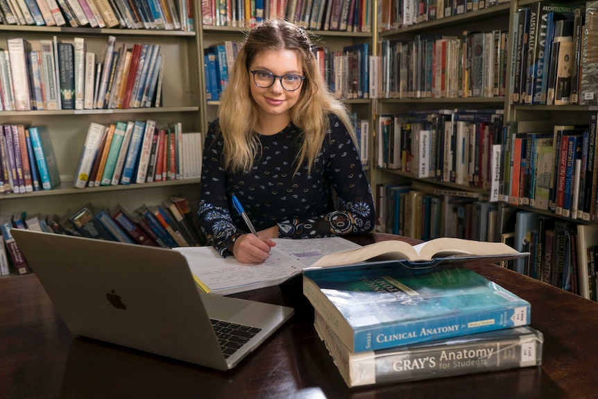 Jasmyn Lloyd studies at a desk, surrounded by books.