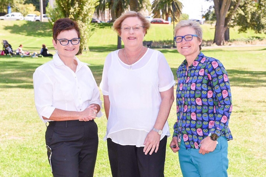 Three women stand together smiling.