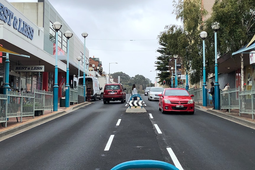 Cars drive on a two-lane street lined with shops