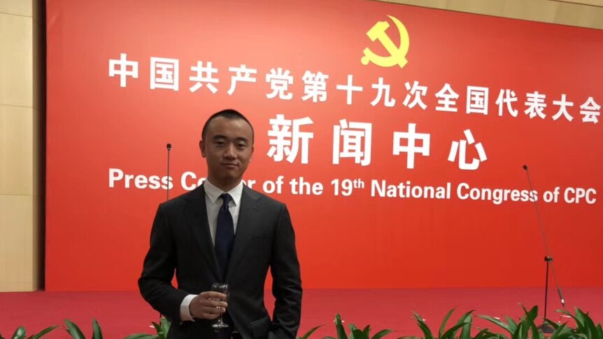 Young man in suit with a wine glass in front of a communist party banner
