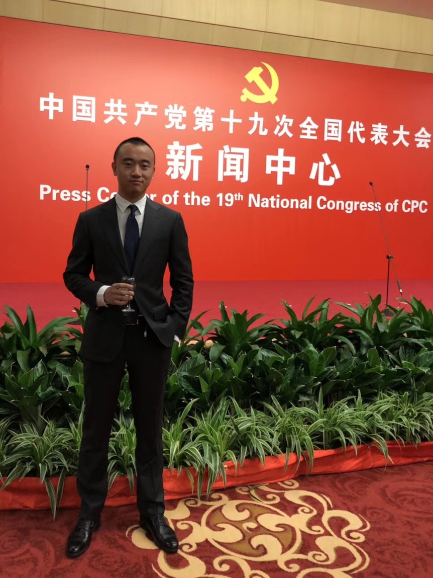 Young man in suit with a wine glass in front of a communist party banner