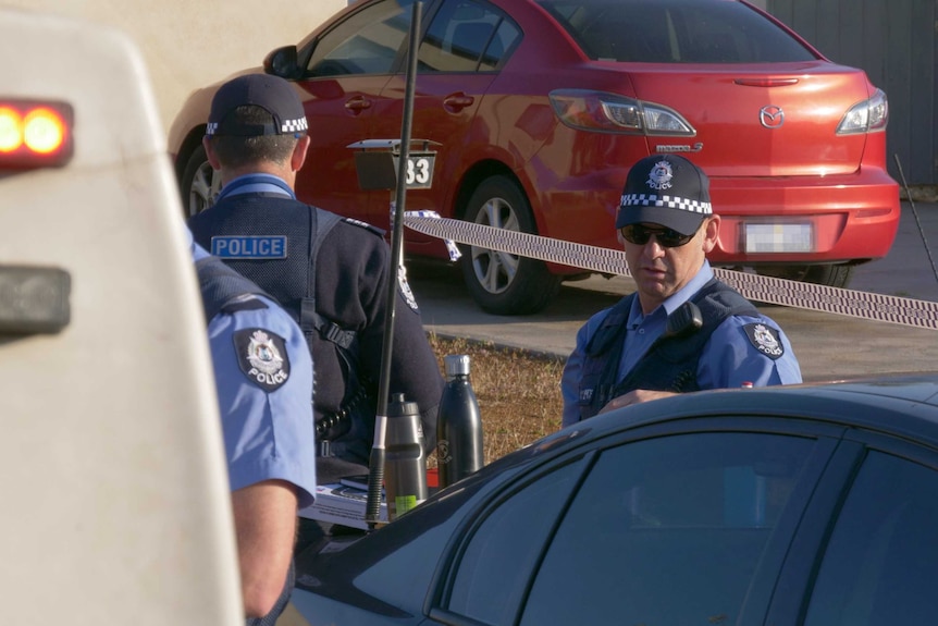 A close-up shot of two police officers in front of a red car.