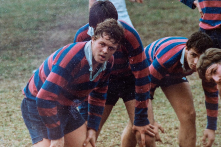 A teenager in a red and blue striped jersey plays rugby union.