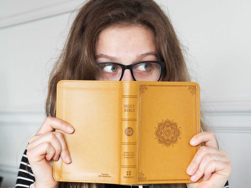 A young women with glasses hiding behind the bible