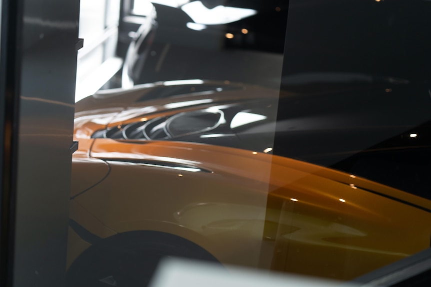 An orange sports car parked in a garage seen through glass