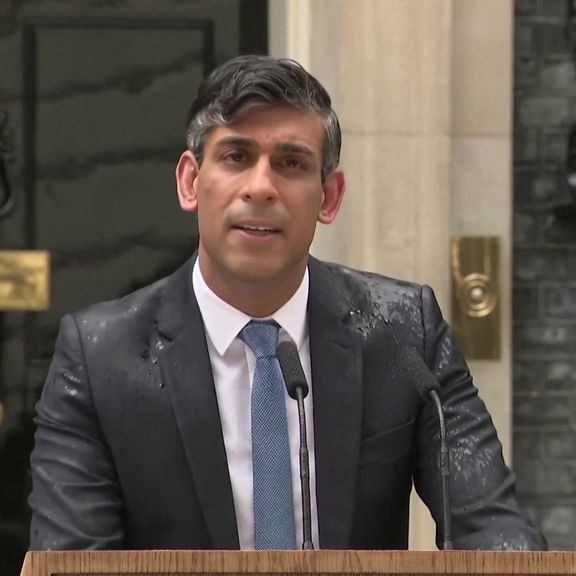 A man in a wet suit speaks into microphones at a lectern.