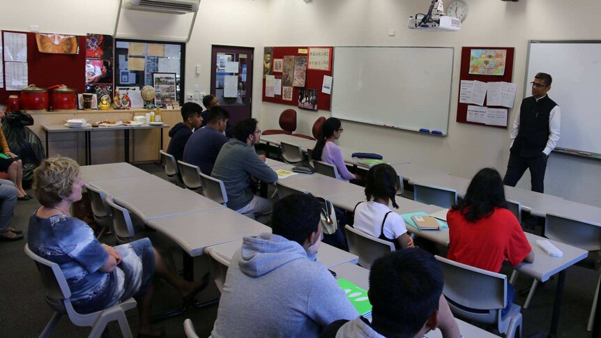 Students sitting in a class with a teacher standing in front of them