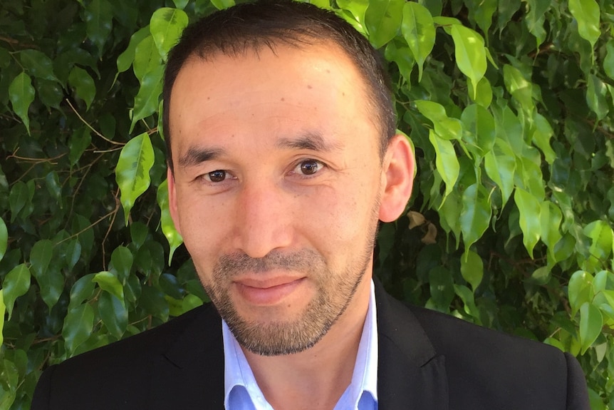 A man in a suit poses in front of a hedge