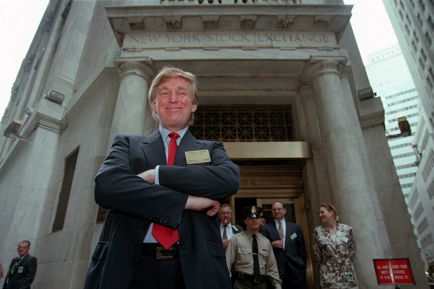 A young Donald Trump stands with his arms folded outside a building that says NEW YORK STOCK EXCHANGE