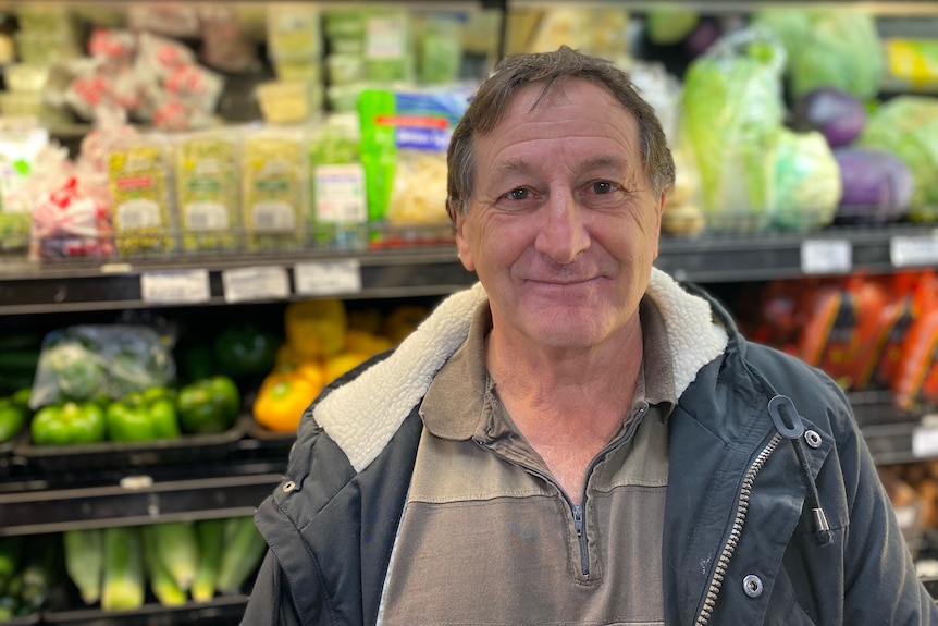 Homme debout devant des produits frais en regardant la caméra 