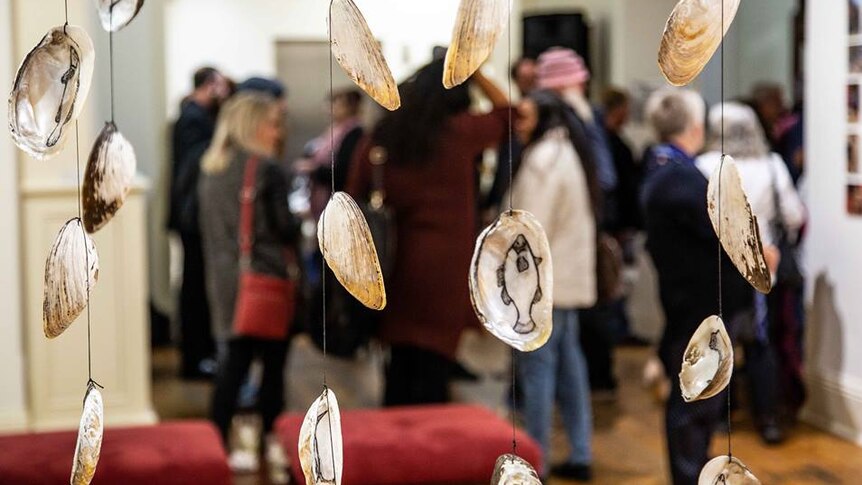 Mussel shells with fish and birds carved in to them hang from string.