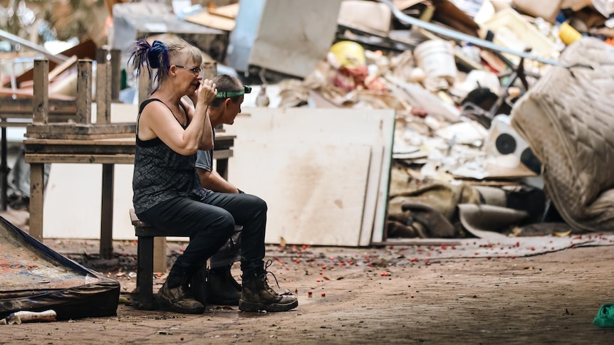 an exhausted woman sits next to piles of rubbish